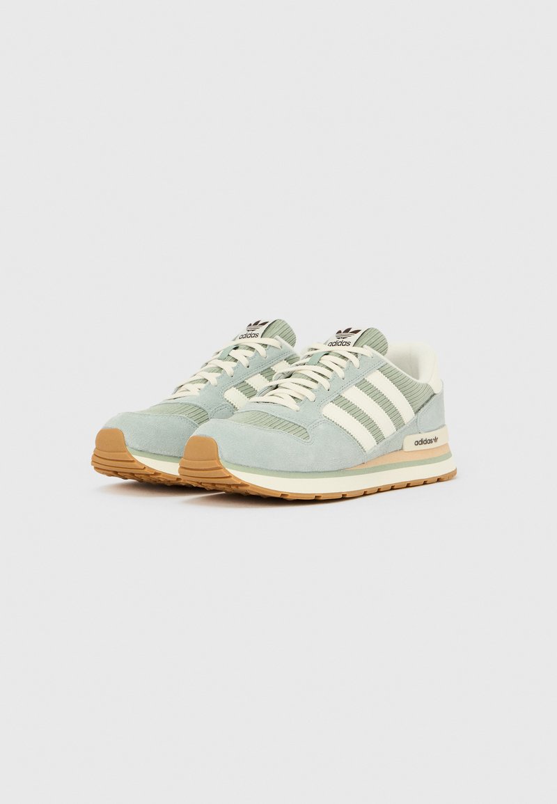 Paire de baskets Adidas vert clair et beige avec des bandes blanches et des semelles couleur gomme sur un fond blanc uni.