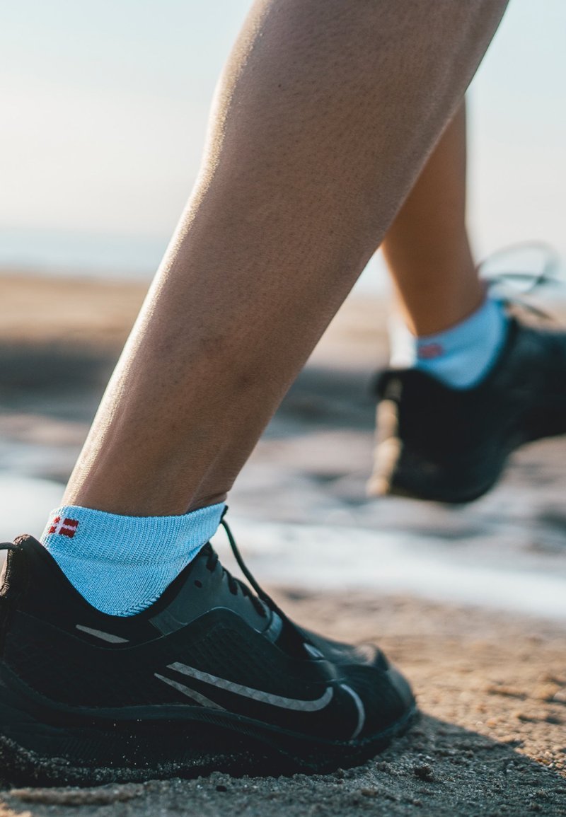 Svarta sportskor med en strömlinjeformad design och grå detaljer, och ljusblå ankelsockor med ett litet rött mönster.