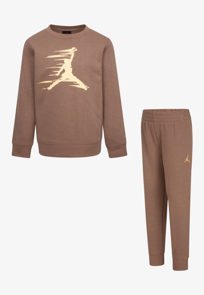 Rudos spalvos sportinė palaidinė ir jos atitinkančios kelnės. Palaidinė turi auksinį Jumpman logotipą, raštuotas rankoves ir apatinę dalį. Kelnės turi elastinę juostelę.