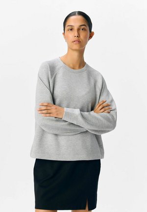 Sweatshirt gris avec des manches raglan, texture douce, col ras du cou et coupe décontractée, associé à une jupe noire avec une fente latérale.