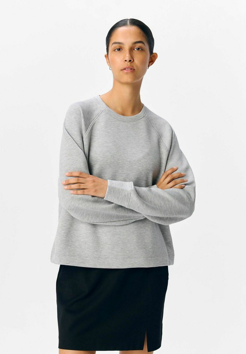 Grijze sweatshirt met raglanmouwen, zachte textuur, ronde hals en een relaxte pasvorm, gecombineerd met een zwarte rok met een zijslit.