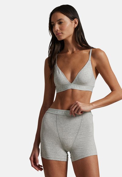 Γυναίκα που φοράει ανοιχτό γκρι bralette Polo Ralph Lauren και ταιριαστό boxer σορτς, στάσιμη μπροστά σε μια απλή φόντο.