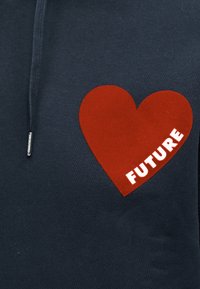 Mørkeblått stoff med en stor rød hjertegrafikk og ordet «FUTURE» i hvite bokstaver inne i hjertet.