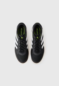 Pair of black Adidas Predator indoor soccer shoes with white stripes and green insoles, viewed from above on a white background.