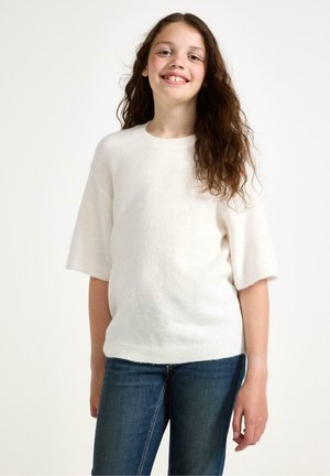 Vit stickad tröja med korta ärmar, rund hals och mjuk textur, ihopparad med blå denimjeans. Sammanfattningsvis en avslappnad outfit.