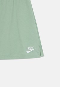 Gaiši zaļš Nike T-krekls, izgatavots no mīksta auduma, ar baltu logotipu apakšējā kreisajā stūrī un sānu izgriezumiem brīvākai kustībai.