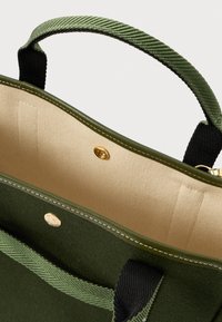 Borsa tote verde e beige con manici neri, chiusura a scatto dorata e cuciture a contrasto sui bordi in tessuto e pelle.