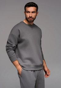 Sudadera gris con cuello redondo y puños acanalados, hecha de una tela texturizada, combinada con pantalones a juego. Diseño simple y minimalista.