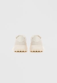 Baskets de couleur claire avec une tige texturée, un col rembourré et une semelle épaisse à crampons. Design minimaliste avec un logo discret au niveau du talon.