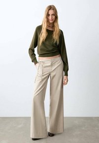 Olivově zelený pletený svetr s krátkým střihem, v kombinaci s volnými béžovými kalhotami se stahovací šňůrkou a širokými nohavicemi. Hladká textura.