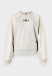 Sweatshirt gris avec des manches raglan crème, arborant un petit logo brodé "Tommy HILFIGER" sur la poitrine. Poignets et ourlet côtelés.