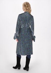 Pitkä, kietaisutyyppinen sininen viitta, jossa on vihreä paisley-kuvio. Valmistettu pehmeästä kankaasta, jossa on leveät hihat ja yhteensopiva vyö. Mustat korot.
