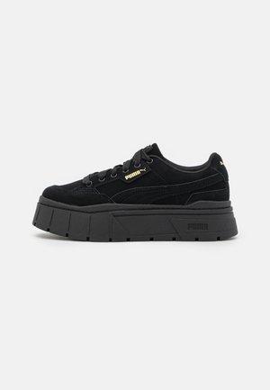 Zapatilla negra Puma con suela gruesa de plataforma, diseño con cordones y logotipo dorado de Puma en el lateral y la lengüeta del talón.