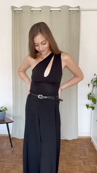 Μαύρη φόρμα με σχέδιο ενός ώμου και άνοιγμα σε σχήμα κλειδιού. Διαθέτει μαύρη ζώνη και φαρδιά πόδια, φτιαγμένη από λείο, ελαστικό ύφασμα.