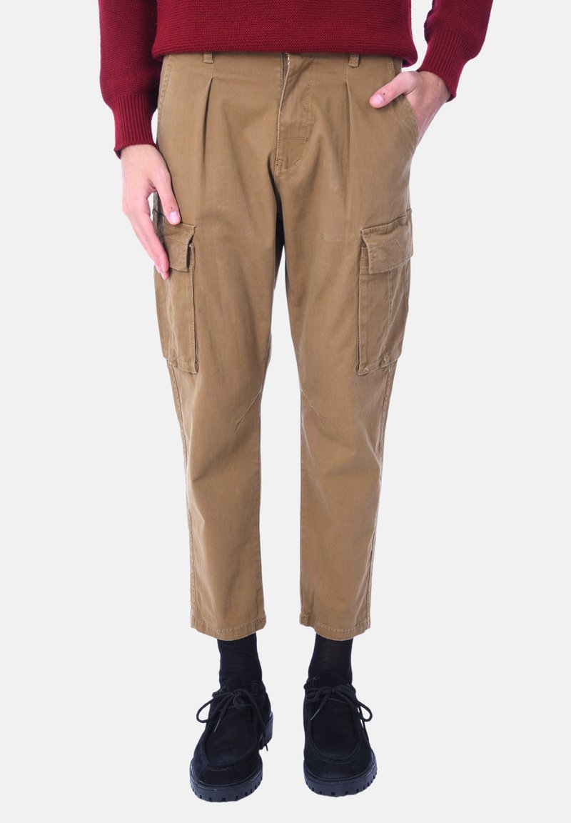 Pantaloni cargo marroni con pieghe, due tasche laterali e vestibilità affusolata. Indossati con scarpe nere e calze, completati da un maglione rosso.