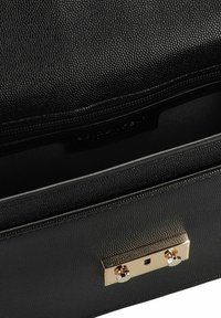 Borsa in pelle nera testurizzata con un clasp in metallo dorato e due accenti rotondi. L'interno è foderato in tessuto scuro e presenta un comparto con zip.