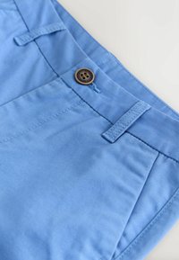 Pantaloni di cotone celeste con una texture liscia, caratterizzati da un bottone marrone e dettagli cuciti in vita e sulle tasche.