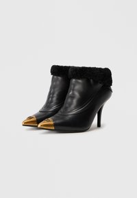 Botas de tacón alto de cuero negro con punta dorada, puño de piel negra y costura decorativa en la parte superior. Diseño texturizado y elegante.