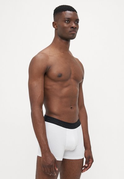 Hvide bomulds boxer briefs med en sort elastisk talje, der har et logo. Stoffet er glat og tæt siddende, båret af en mandlig model.