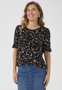 Blouse noire avec un motif abstrait beige, manches courtes bouffantes, encolure plissée, tissu léger, associée à une jupe en denim.