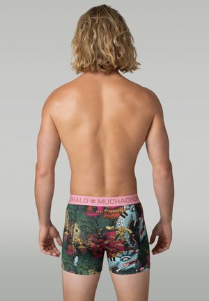 Achteraanzicht van een shirtloos persoon die kleurrijke boxer briefs draagt met een roze tailleband en ingewikkelde jungle- en dierenpatronen.