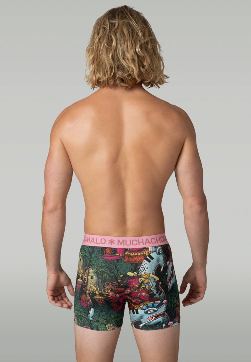 Zadnji pogled na osebo brez srajce, oblečeno v pisane boksarske hlače z roza pasom in zapletenimi vzorci džungle in živali.