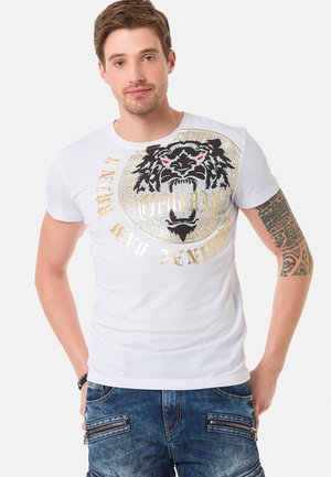 Weißes T-Shirt mit kurzen Ärmeln, das ein schwarzes und goldenes Löwenmotiv mit roten Akzenten und stilisiertem Text zeigt. Glatte Oberfläche, figurbetonte Passform.