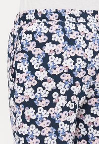 Un pantalon à imprimé floral présente un fond marine avec des motifs de fleurs rose clair et bleus, une taille élastique et des poches latérales.