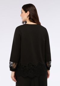 Top nero con maniche lunghe, caratterizzato da dettagli in pizzo ai polsini e un orlo in pizzo scallop. Tessuto liscio con una texture raffinata.