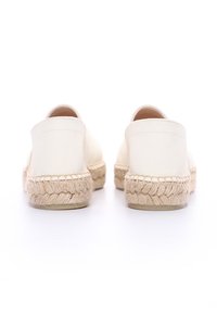Espadrilles en toile blanche avec une semelle intermédiaire en jute tressé, présentant un dos fermé et un design plat. Texture lisse et silhouette simple.