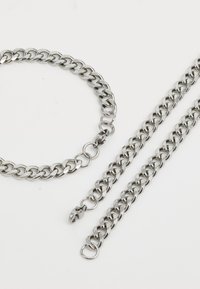 Sølvmetal kædesmykkesæt bestående af et tykt halskæde og to armbånd, karakteriseret ved sammenflettede led og en poleret overflade.