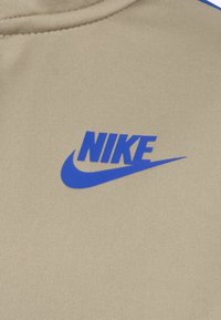 Bežna tkanina z teksturirano površino ima modri logo "NIKE" in grafiko swoosh, ki je postavljena na sredini.