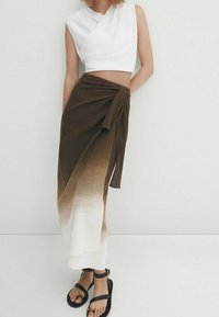 Haut court blanc au design asymétrique, associé à une jupe dégradée marron vers blanc, avec un détail noué, et des sandales noires.