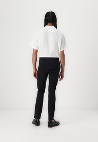 White short-sleeve shirt made of light fabric, paired with black slim-fit pants. Soft texture with clean lines and minimal detailing. Black shoes.