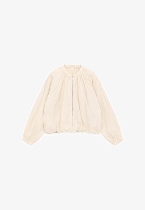 Veste courte beige avec un col rond, des poignets élastiques et une fermeture éclair frontale. Confectionnée dans un tissu léger à la texture lisse.
