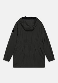Giacca leggera nera con cappuccio, vita elastica e maniche lunghe. Presenta una superficie liscia e una piccola etichetta del marchio sulla manica.