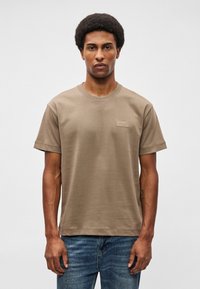 Barna, rövid ujjú póló kerek nyakkivágással és téglalap alakú címkével a mellkasán. Puha tapintású, laza fazonú, kék farmernadrággal párosítva.