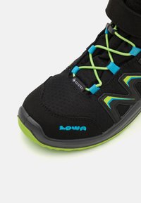 Melnas pārgājienu kurpes ar Gore-Tex materiālu, ar spilgti zaļām un zilām auklām, mīkstu zoli un "LOWA" logo zilā krāsā sānos.