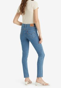 Světlé modré džínové kalhoty s vysokým pasem a přiléhavým střihem, s viditelnými zadními kapsami a hnědou koženou značkovou nášivkou na pase.