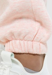 Lichtroze, gestructureerde sweatpants met bijeen geraapte manchetten, gedragen met een witte sneaker met een gaasontwerp en pastelaccent bij de veters.