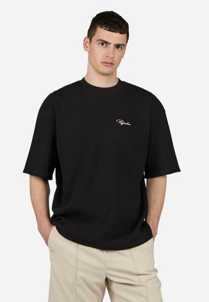 Black waffle-knit oversized t-shirt with short sleeves and a round neckline, featuring a small white logo on the left chest.