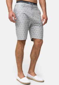Shorts gris à motif géométrique, avec une ceinture noire INDICODE. Associés à des chaussures blanches à enfiler.