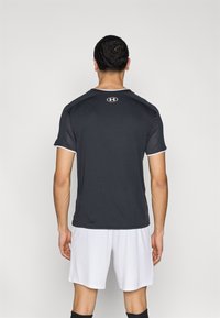 Μαύρο αθλητικό μπλουζάκι με κοντά μανίκια, με λευκές λεπτομέρειες και λογότυπο στην πλάτη. Φορεμένο με λευκό σορτς, με λεία υφή.