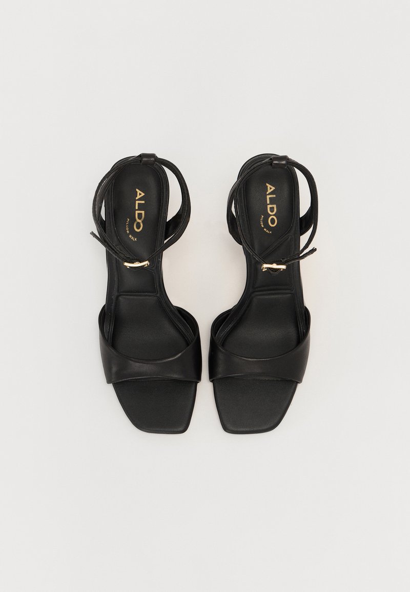 Sandales à talons en cuir noir avec un design à bout carré, une fine lanière à la cheville et une surface lisse, présentant un logo sur la semelle intérieure.