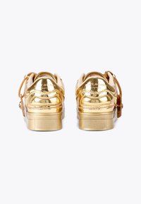 Sneaker metallic dorate con una finitura liscia, colletto imbottito, dettagli decorativi e suole texturizzate. Presenta il marchio sul retro.