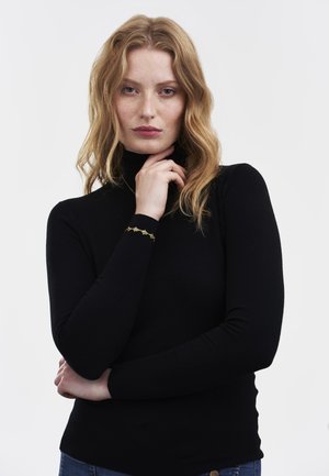Pull à col roulé noir avec des manches longues, design ajusté et texture côtelée. Présente un accent décoratif doré sur le poignet gauche.