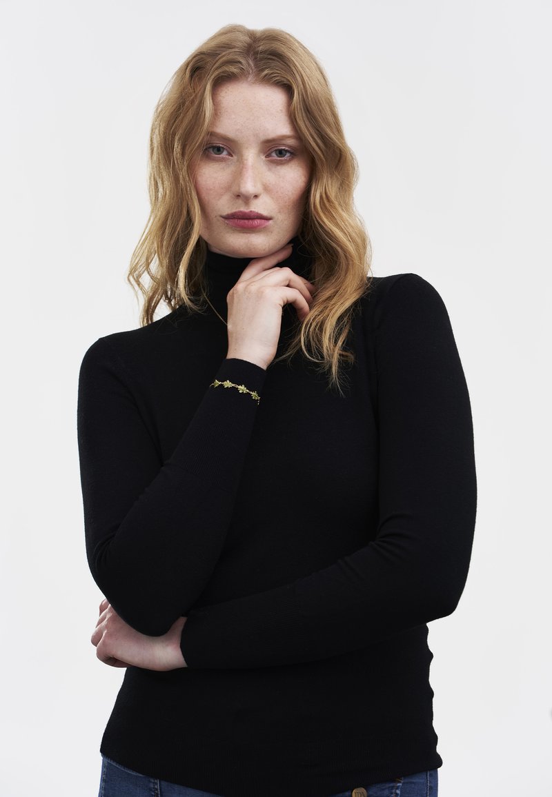 Black turtleneck sweater with long sleeves, fitted design, and ribbed texture. Features a decorative gold accent on the left wrist.