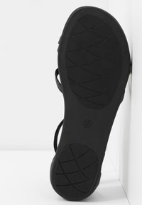 Schwarze Sandalensohle mit strukturiertem Oberflächen- und Griffmuster. Größe gekennzeichnet als 37. Riemen erstrecken sich von der Sohle und zeigen ein offenes Design.