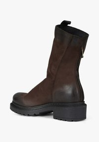 Stivaletto marrone in pelle con finitura strutturata, cerniera laterale e suola in gomma nera spessa. Dotato di un anello sulla parte superiore per facilitare la calzata.