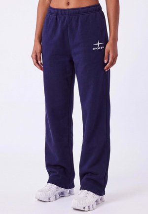 Pantalon de jogging bleu marine avec taille élastique et logo blanc "PXP", porté avec des chaussures de sport blanches sur une personne debout.